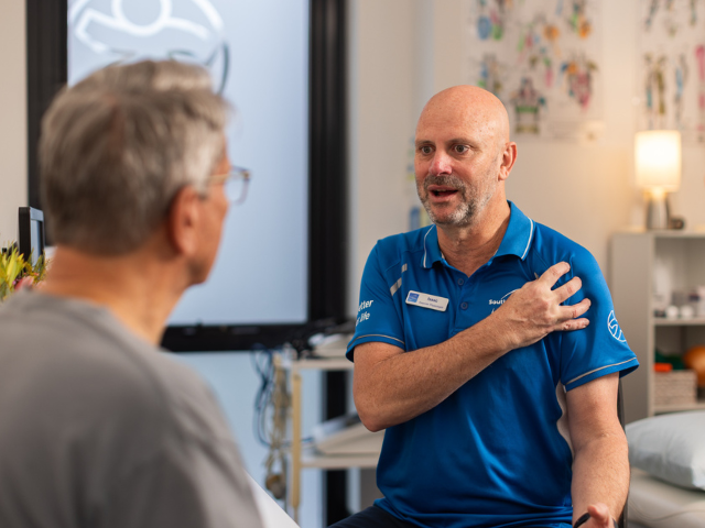 Southern Cross Care Male Allied Health Professional Consulting With Male Home Care Client.