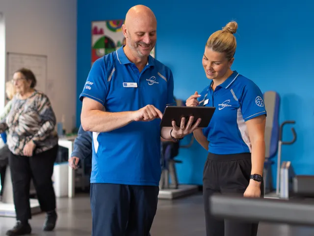 Male and Female Southern Cross Care Allied Health Staff Members Looking At Tablet Together In Carmelite Health & Fitness Centre