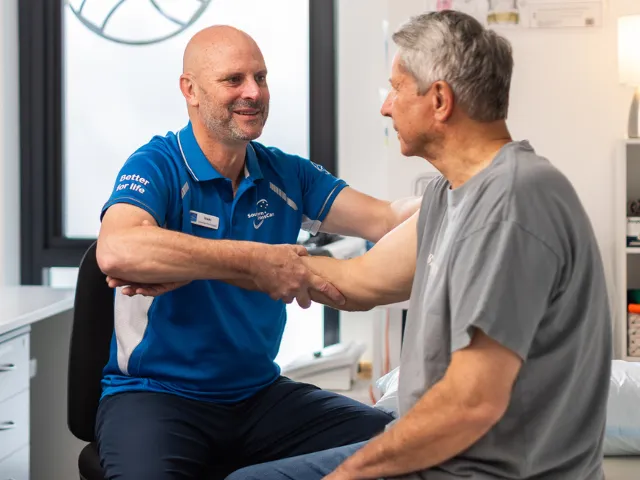 Southern Cross Care Male Allied Health Professional Consulting With Male Home Care Client