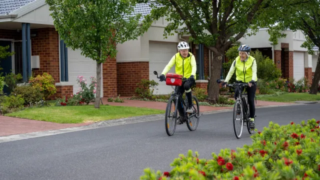Female and Male Resident Riding Bikes On Street At Bedford Heights Estate Retirement Living