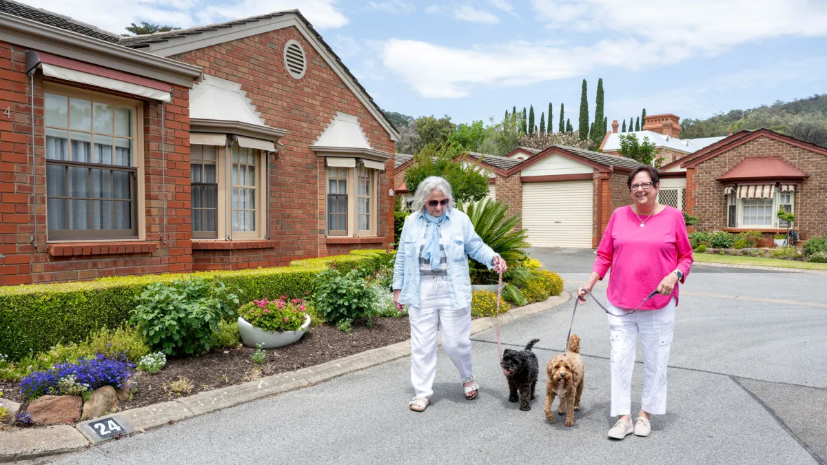 Two Female Residents Walking Dogs At Retirement Village