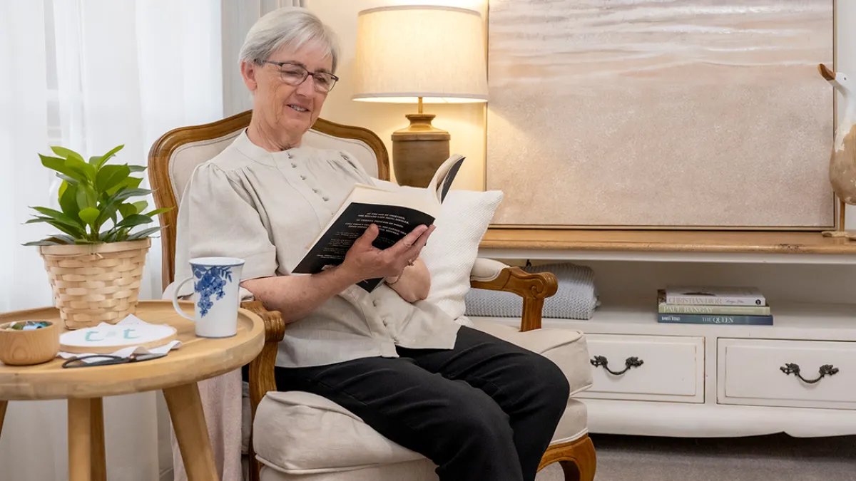 Female Resident Reading Book In Lounge Room