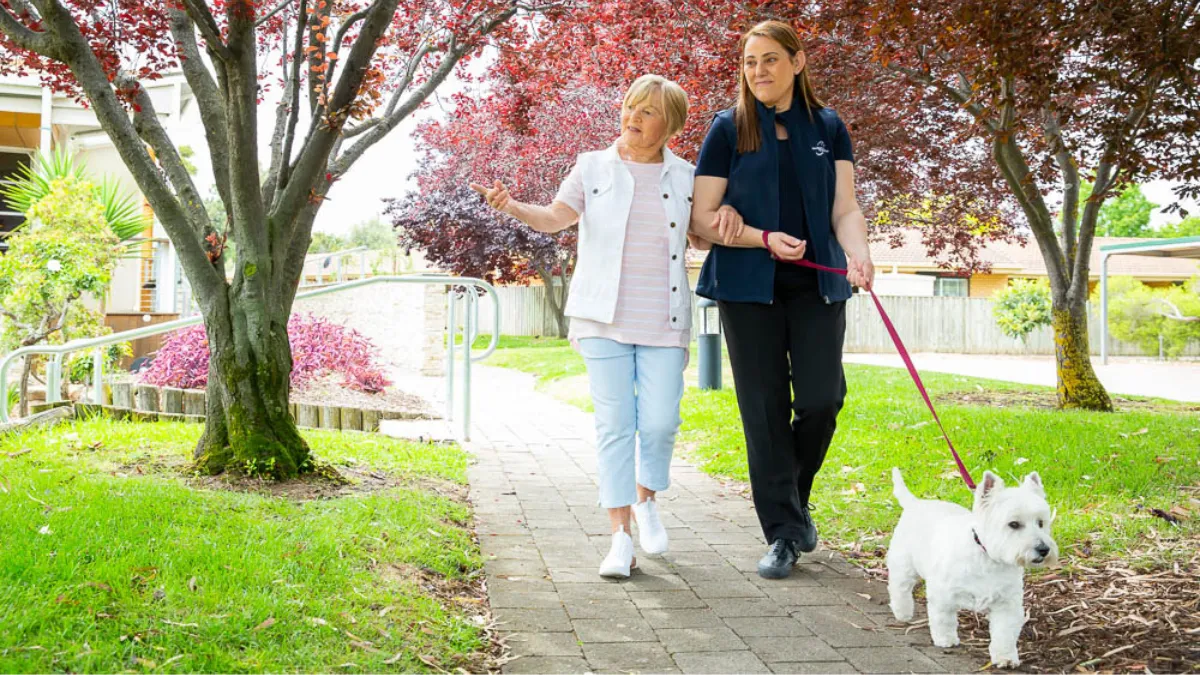 Home Care Client And Home Care Staff On Walk With Dog