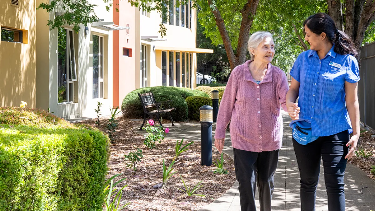 A resident and staff member walking in the garden