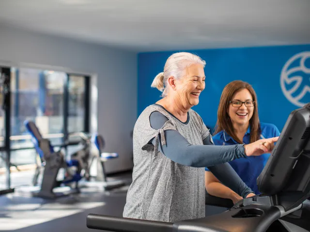 Carmelite Health & Wellness Lady with instructor in gym  An older female client performing a bicep curl with a dumbbell, receiving professional guidance and support from an Accredited Exercise Physiologist
