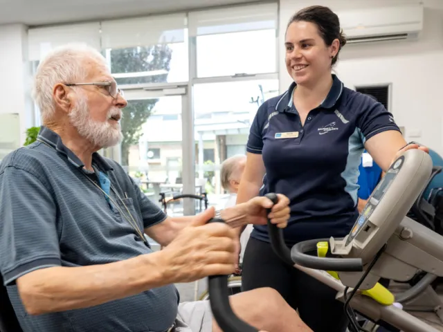 Male Resident On Exercise Machine With Assistance From Female Allied Health Staff Member At The Phillip Kennedy Centre Residential Care