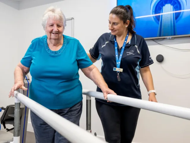 Female Resident On Exercise Machine With Assistance From Female Allied Health Staff Member At Carmelite Residential Care