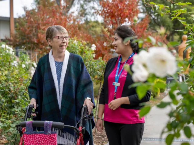 Female Resident and Female Lifestyle Staff Member Walking Through The Garden Together At Carmelite Residential Care