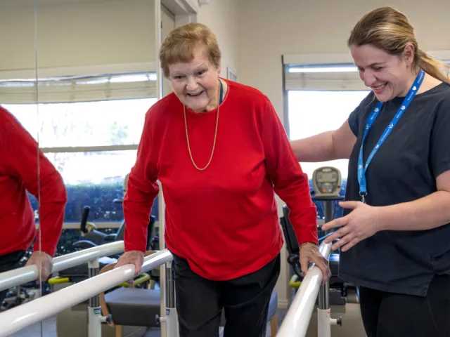 Female Resident On Exercise Machine With Assistance From Female Health & Fitness Staff Member At Oaklands Park Lodge Residential Care