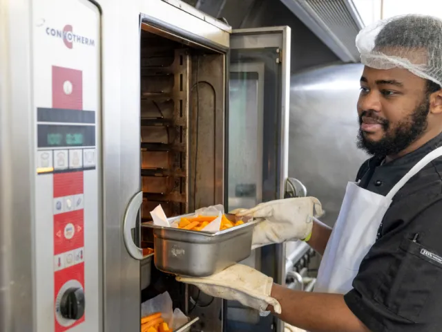 Male Chef Putting Roasted Vegetables Into The Oven At Oaklands Park Lodge Residential Care