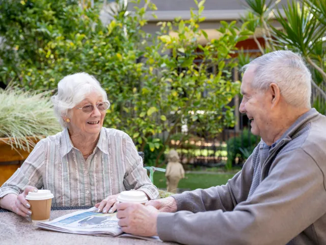 Male and Female Resident Enjoying A Coffee In The Garden Together At Oaklands Park Lodge Residential Care