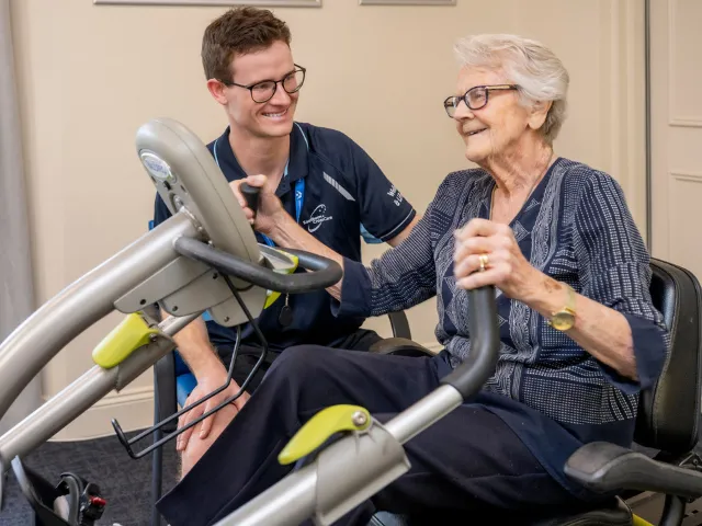 Female Resident On Exercise Machine with Assistance From Health & Fitness staff member 