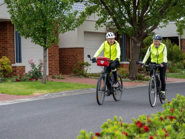 Female and Male Resident Riding Bikes On Street At Bedford Heights Estate Retirement Living