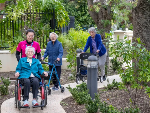 Female support worker walking with 3 residents in the Lourdes Valley Garden