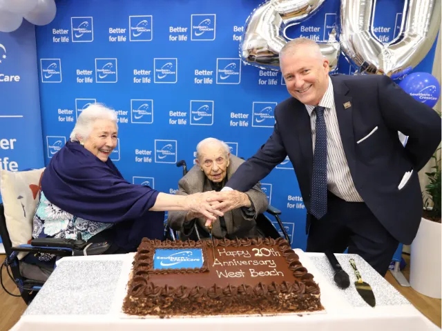 Residents Cathy and Norman cutting the cake with CEO David Moran