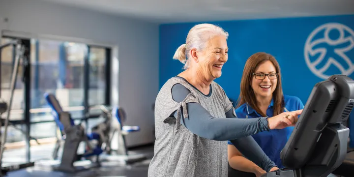 Carmelite Health & Wellness Lady with instructor in gym  An older female client performing a bicep curl with a dumbbell, receiving professional guidance and support from an Accredited Exercise Physiologist