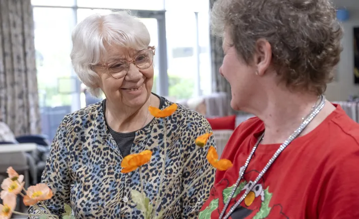 A respite client completes a puzzle while enjoying a cup of tea. Residential Respite Care image: Two female Residential Care residents smile at each other while arranging flowers