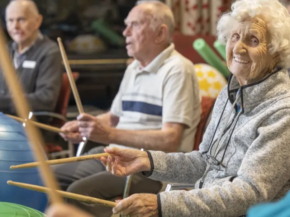 3 residents enjoying a music class with drumsticks in hand