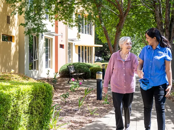 Female Resident and Female Personal Care Worker Walking Together Outside At The Pines Lodge Residential Care