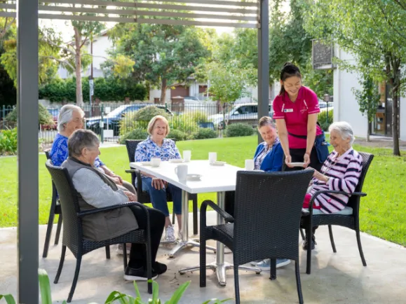 Five Female Residents and Female Lifestyle Staff Member Sitting Outside At Table At Fullarton Residential Care
