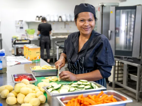 Female Chef Cutting Vegetables With Knife In Kitchen At Southern Cross Care Residential Care Home
