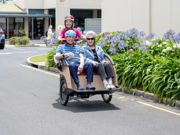 Lifestyle Staff Member and Two Residents On A Trike Bike Outside At Southern Cross Care Residential Care Home