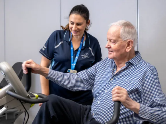 Male Resident Using An Exercise Machine With Female Exercise Physiologist Assistance At At Southern Cross Care Residential Care Home