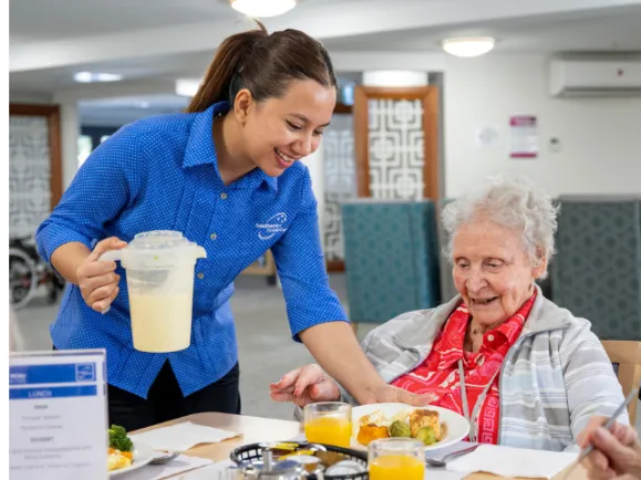 Female Resident Being Served Lunch By Female Personal Care Worker At Mount Carmel Residential Care